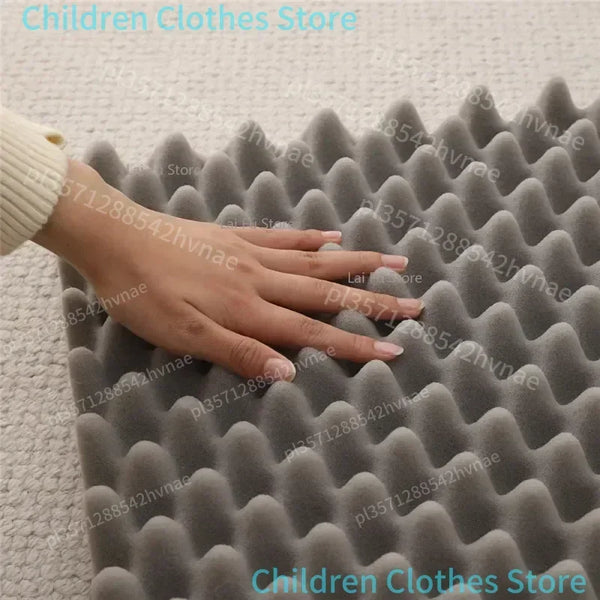 Hand touching a textured gray foam mat on a light-colored floor.

